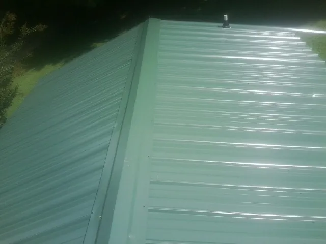 New green metal panels meeting at the ridge of a roof — Flat Roof Repair work by our crew in North Palm Beach