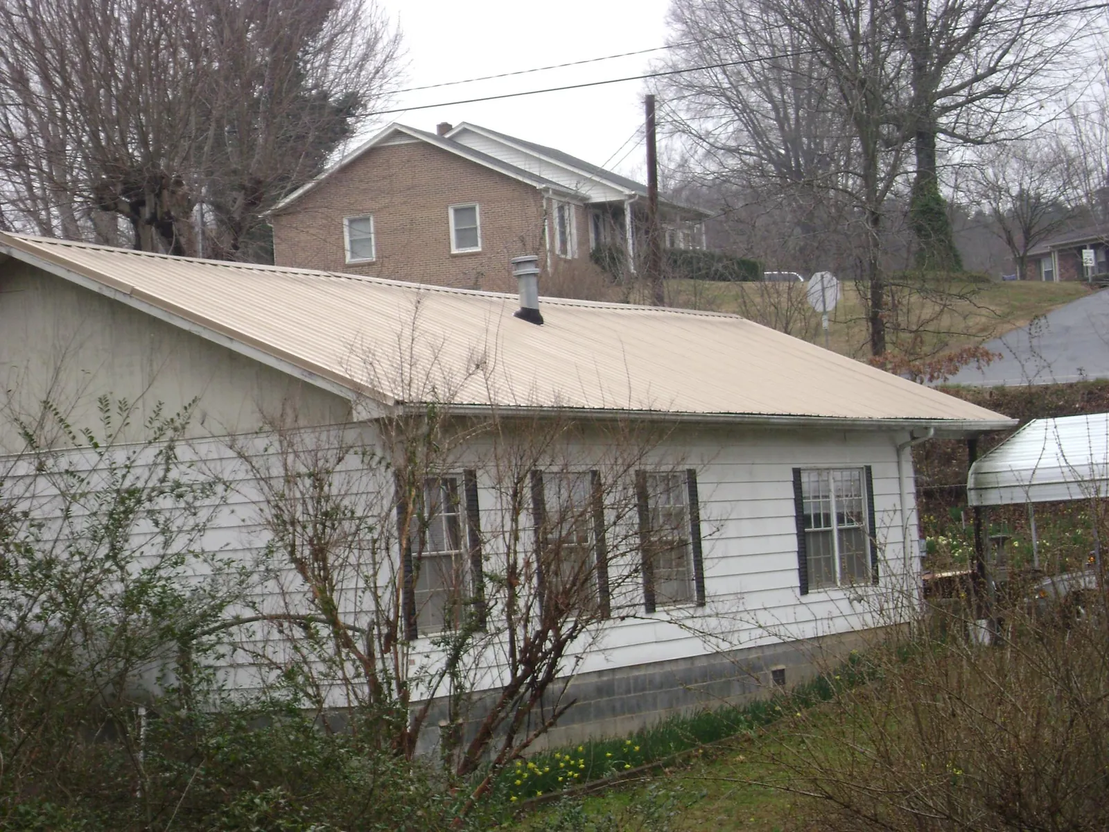 Tan metal roof on a white sided house set into a hillside — Commercial Roofing by Roofing Brothers in North Palm Beach